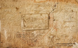 Glaube und Hoffnung: Die Palme ist eine Anspielung auf die biblische Mythologie. Sie steht als Symbol für Sieg und Triumph. Auch im Ghetto Theresienstadt, in dem offiziell die Religionsausübung verboten war, hatten religiöse Symbole des Judentums für Gläubige ihre Bedeutung. Das galt auch für den neunarmigen Leuchter, das Symbol für das Chanukka-Fest (dt. Wiedereinweihung), das die Wintersonnenwende ankündigt. Gefeiert wird der Triumph des Lichts über die Dunkelheit. Im Ghetto war der Chanukka-Leuchter freilich mehr als nur ein religiöses Motiv, denn das Lichteranzünden symbolisiert auch den Sieg des Guten über das Böse und den Neuanfang. Zur Tradition gehört, den Chanukka-Leuchter von der Straße aus sichtbar aufzustellen. Das hatte der Urheber vermutlich im Sinn, als er dieses Motiv in den Sandstein ritzte. Text: Uta Fischer © 2014, All rights reserved